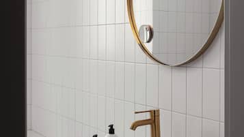 Un baño con lavamanos blanco, grifo dorado y un espejo redondo con marco dorado.