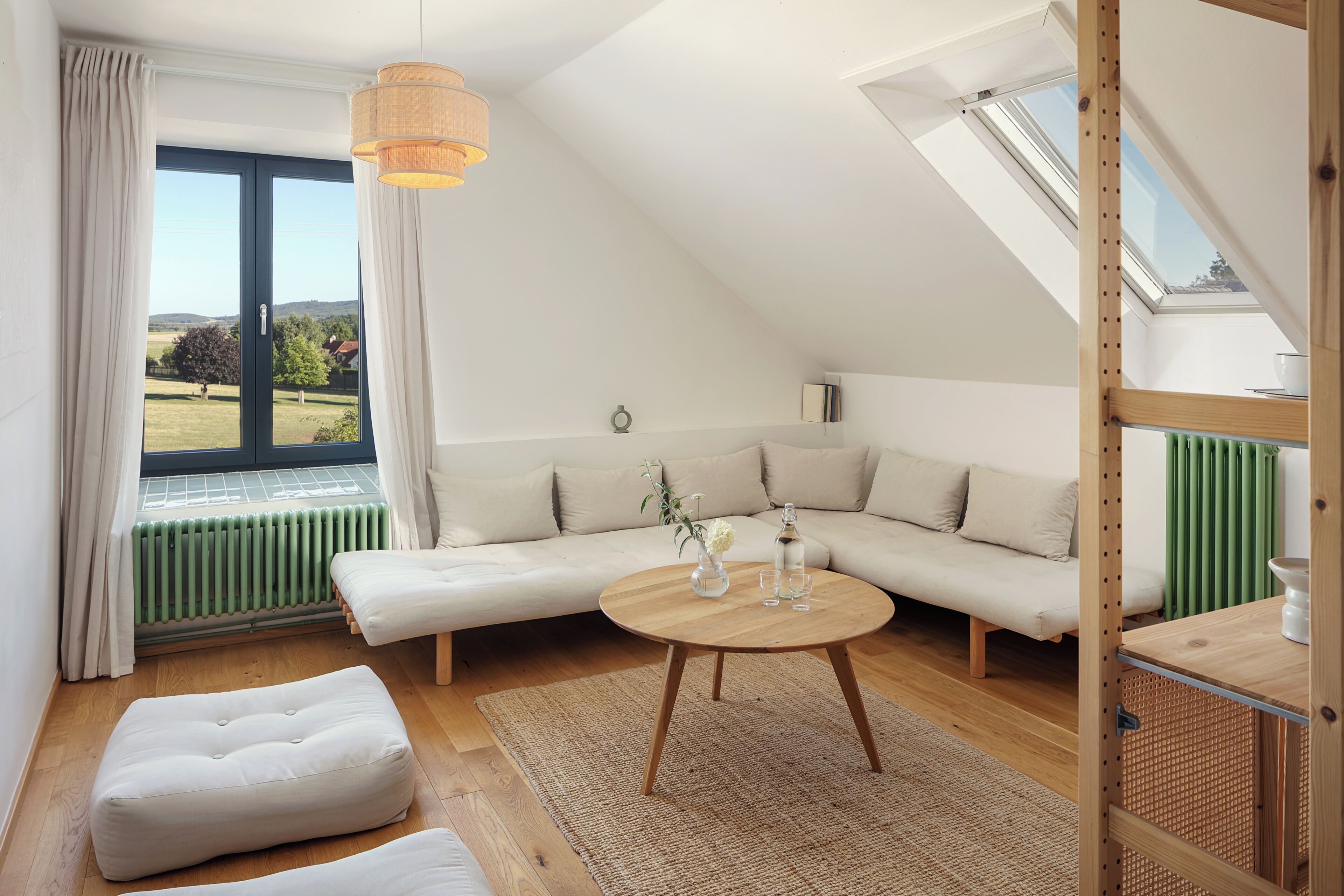 Un dormitorio estilo loft moderno con un gran ventanal, techo de madera, un sofá, una mesa redonda de madera y vistas al exterior.