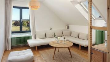 Un dormitorio estilo loft moderno con un gran ventanal, techo de madera, un sofá, una mesa redonda de madera y vistas al exterior.