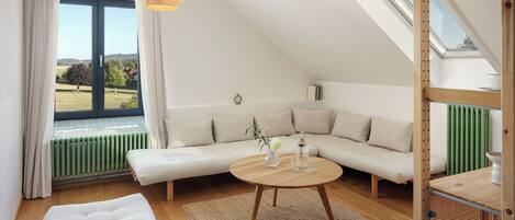 Un dormitorio estilo loft moderno con un gran ventanal, techo de madera, un sofá, una mesa redonda de madera y vistas al exterior.