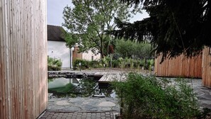 A courtyard with a stone pathway, a small pond, wooden fences, and lush greenery. - po.spolu wellness resort (Mokrovraty)