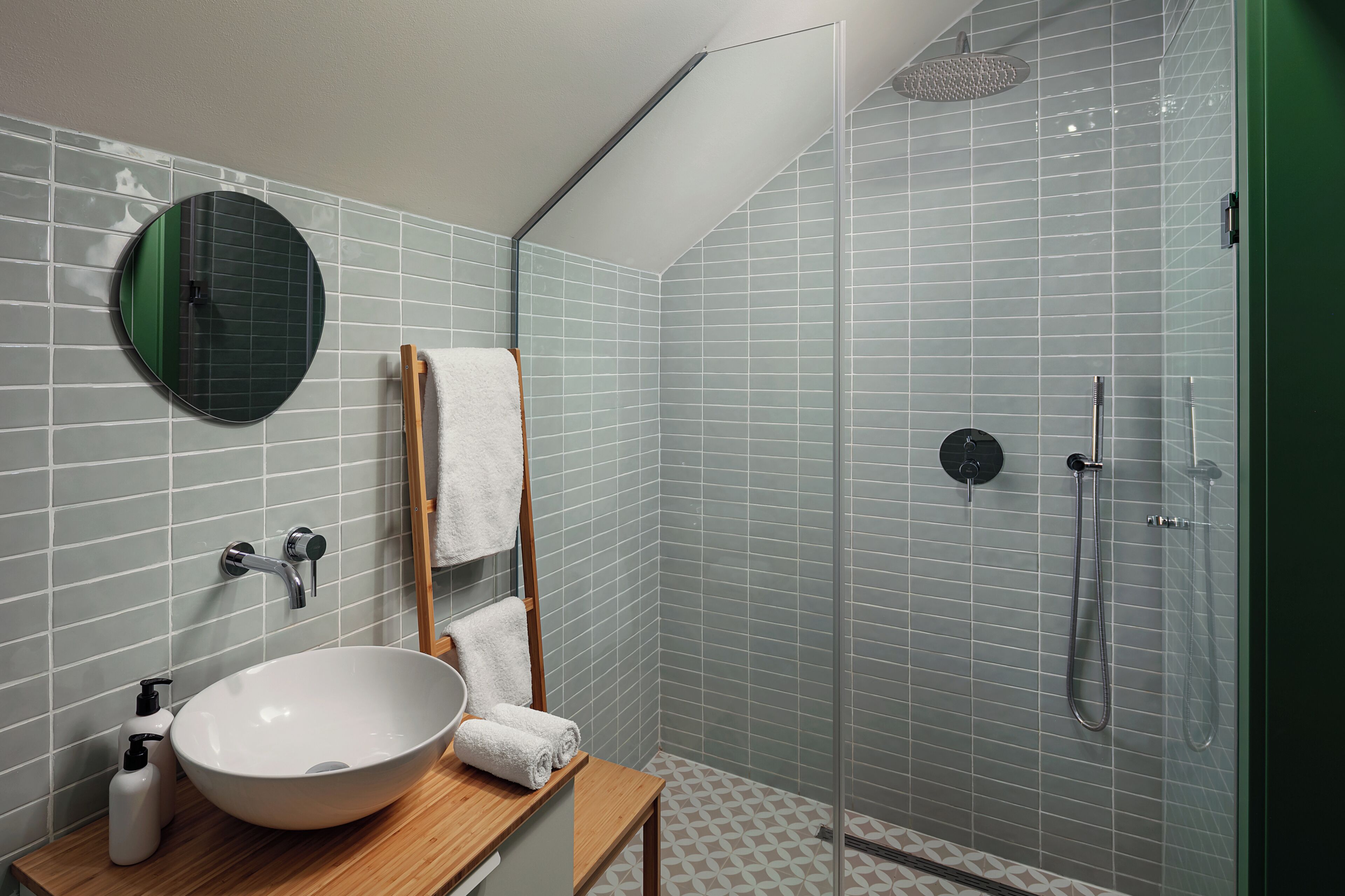 Un baño con un espejo redondo, un lavabo, un perchero para toallas y una ducha.