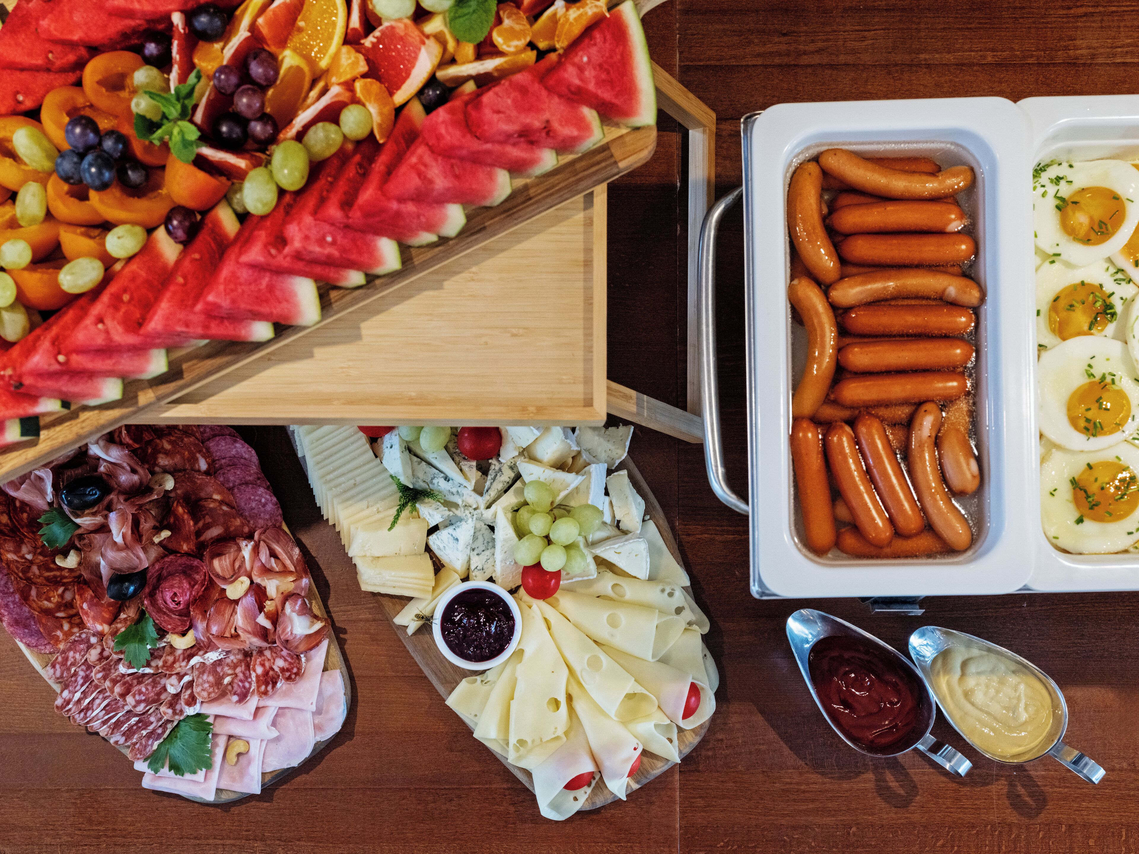 A variety of food items including sliced fruits, cheeses, and meats arranged on a wooden board.