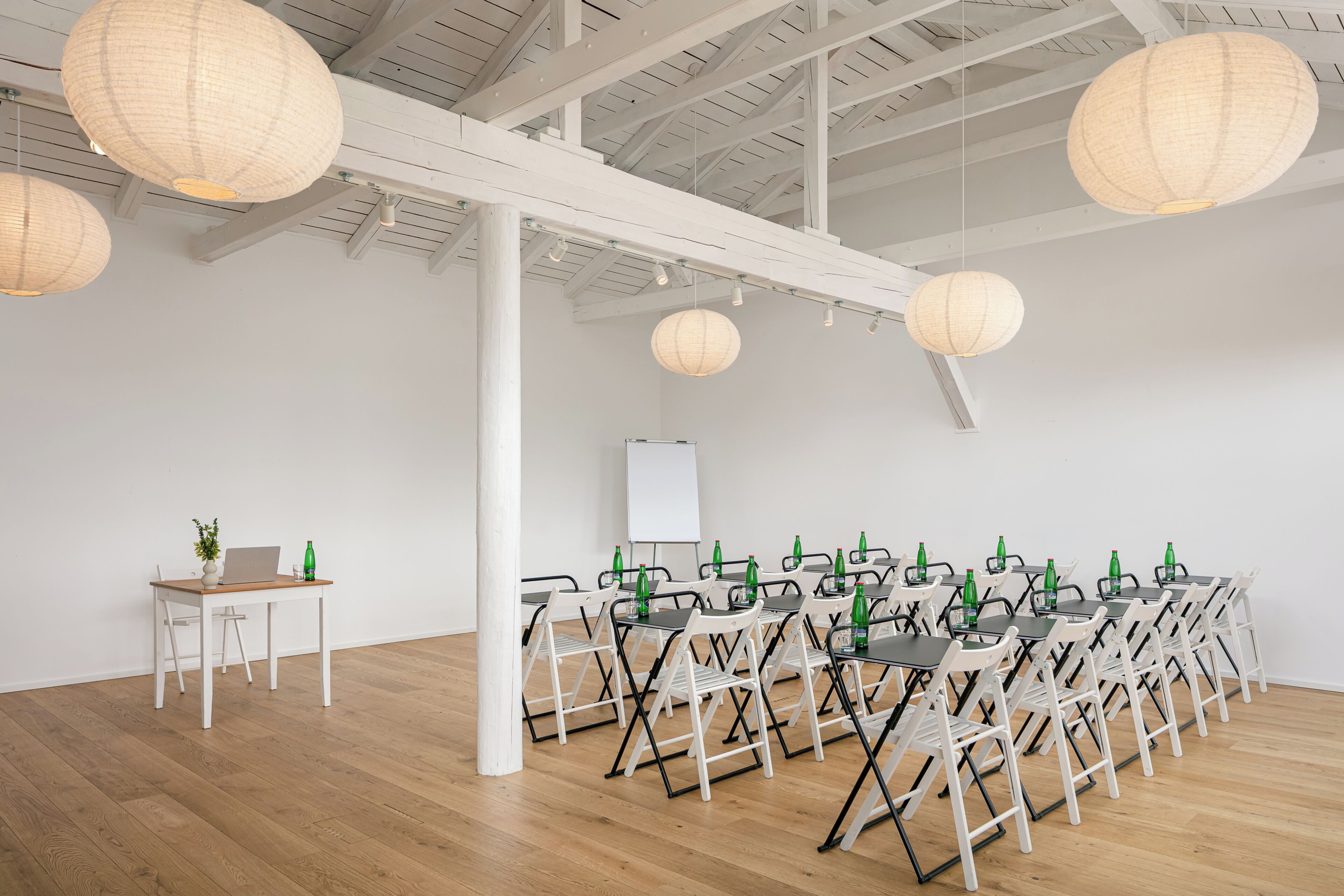 Un salón de conferencias con paredes blancas, pisos de madera y varias mesas con sillas.
