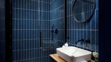 A modern bathroom with a large white sink, a round mirror, and a shower enclosure with blue-tiled walls.
