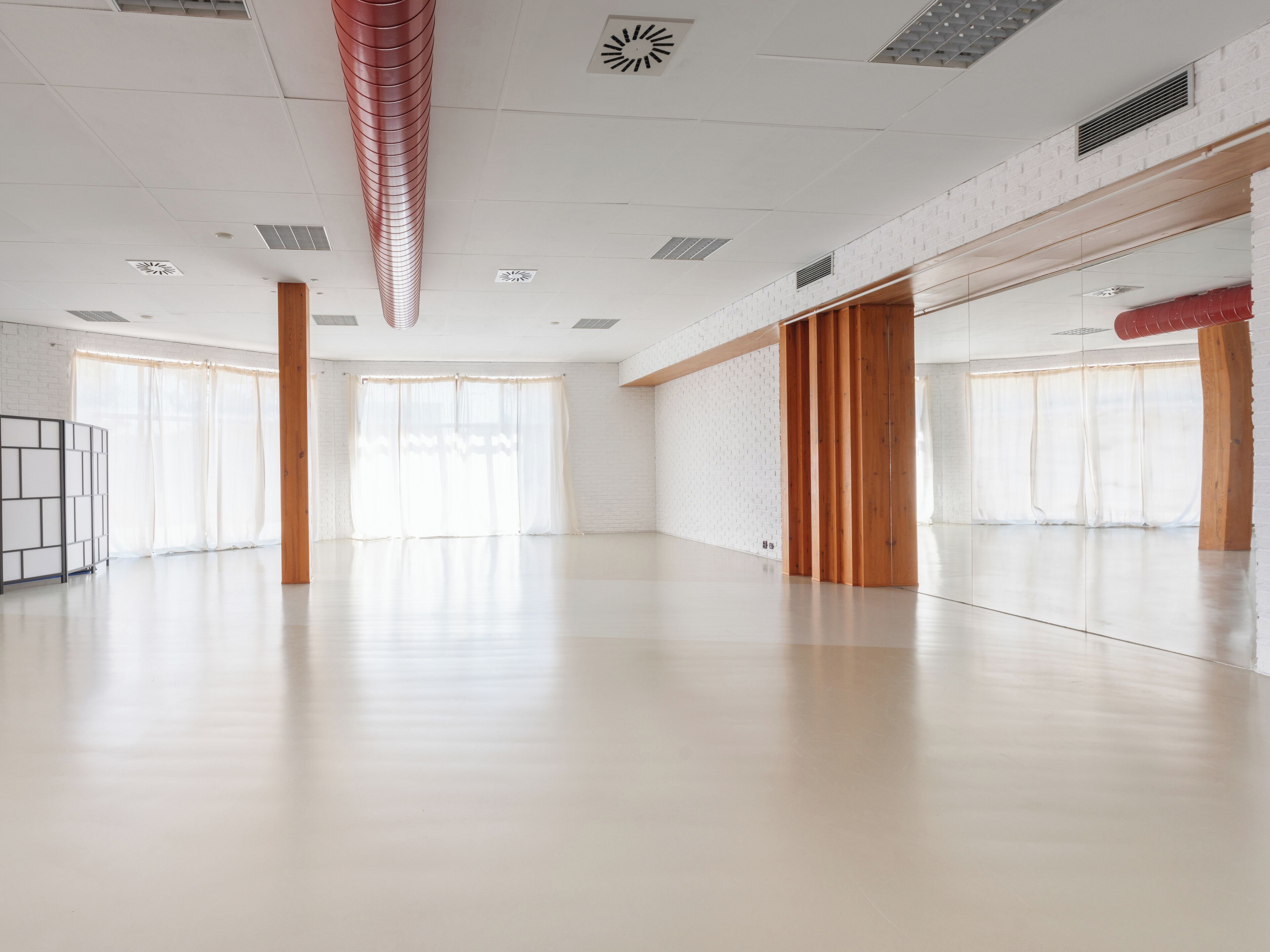 A spacious, modern room with a high ceiling, large windows, and a wooden floor.