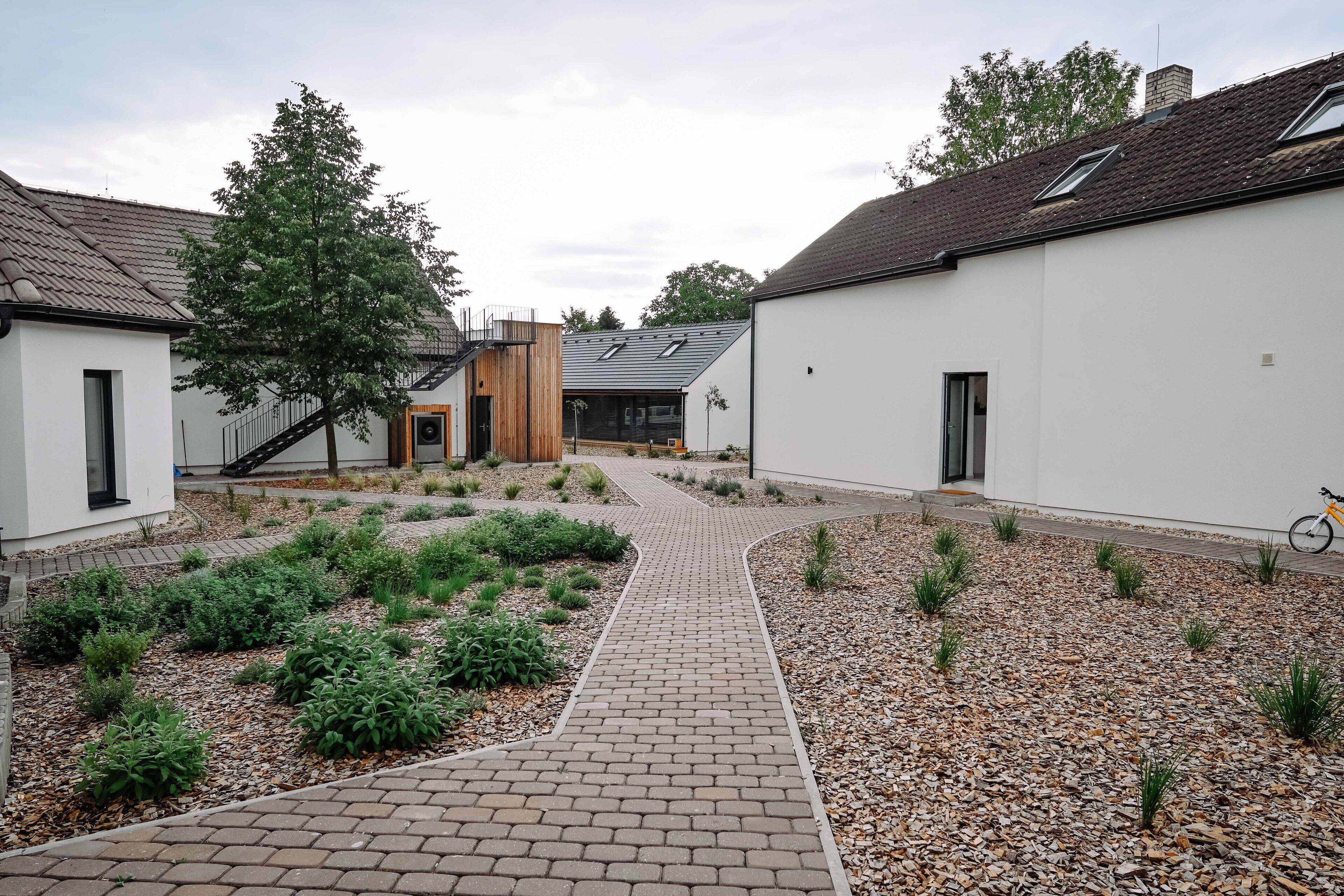 Ein Innenhof mit gepflastertem Weg, umgeben von Gebäuden mit weißen Wänden und Ziegel-Dächern.
