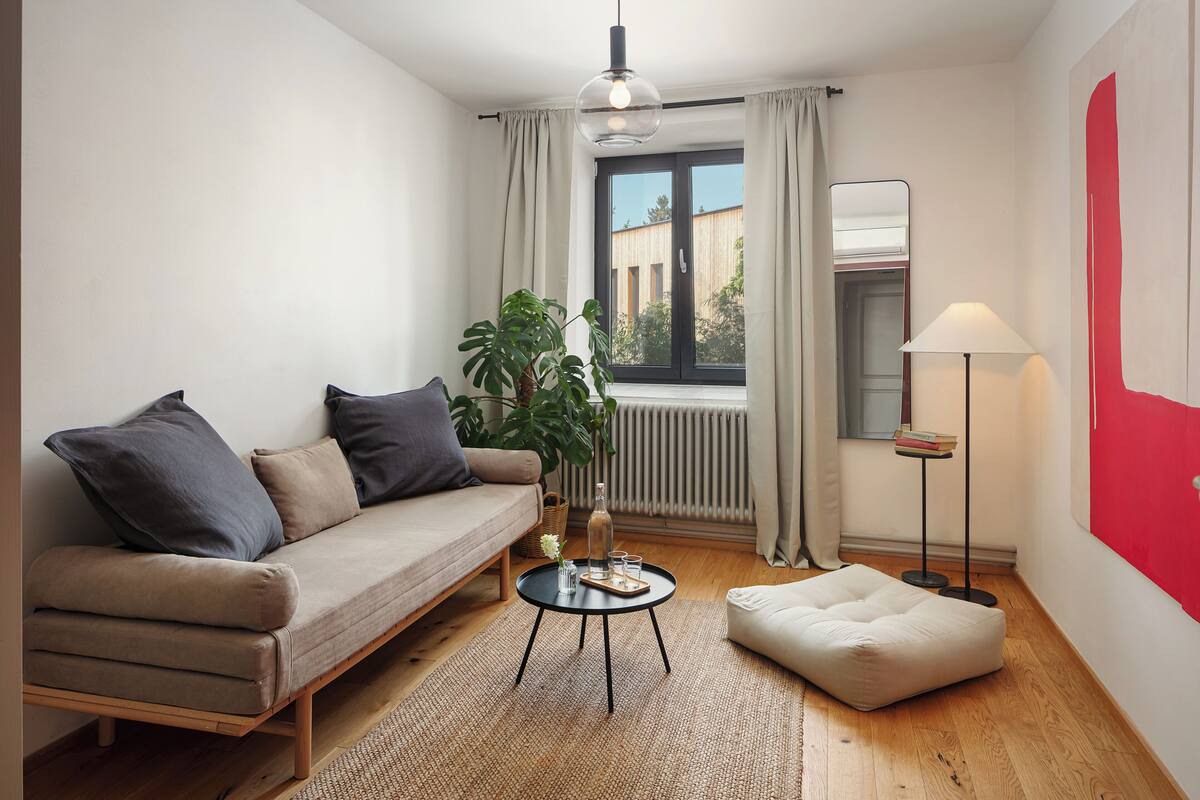A modern living room with a sofa, a small round table, a floor lamp, and a window with curtains.