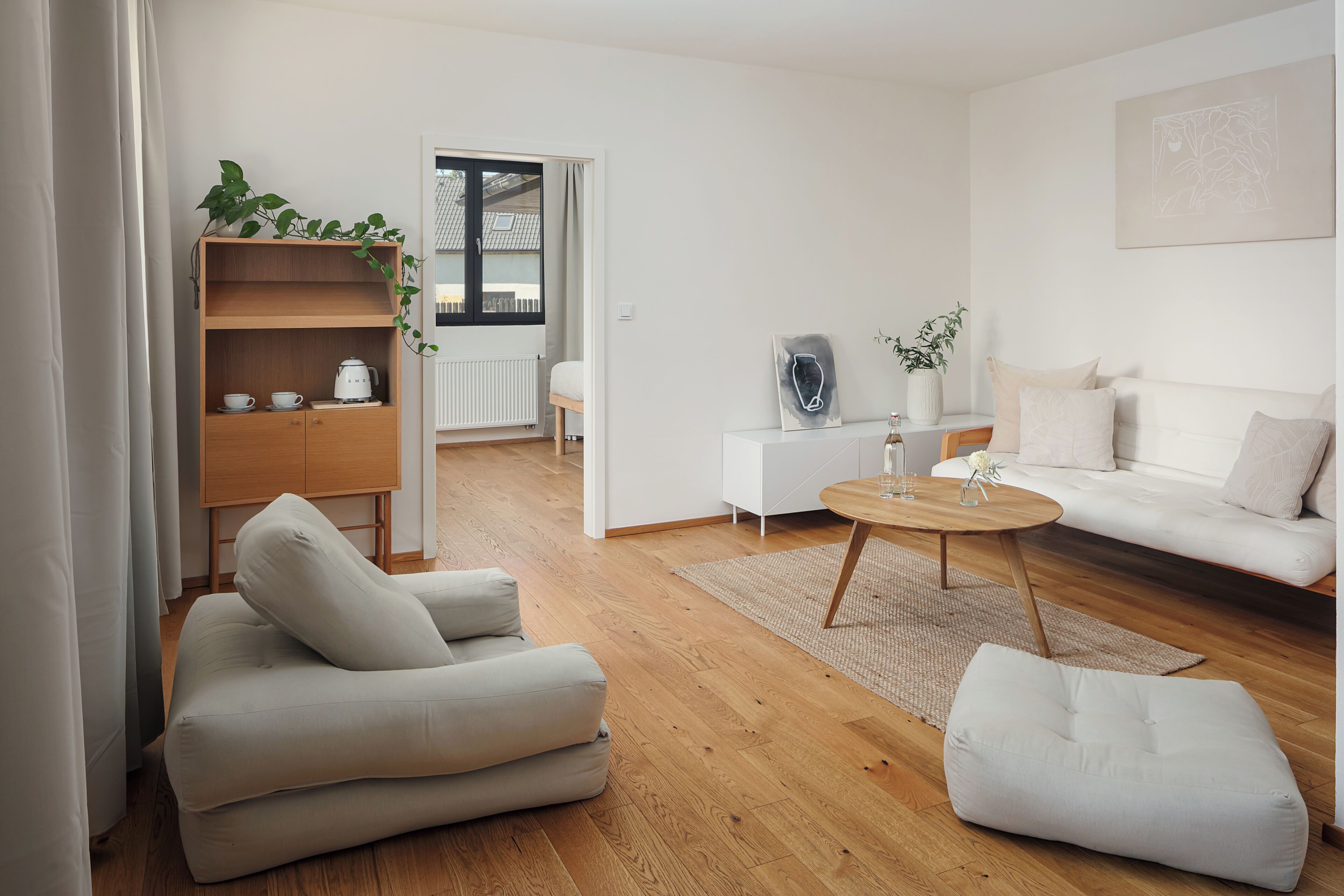 Un salon moderne avec un canapé, un fauteuil, une table basse et une bibliothèque en bois agrémentée de plantes.