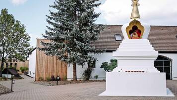 Un stupa blanc surmonté d’une coupole dorée, un bâtiment en bois et un grand arbre à l’avant.