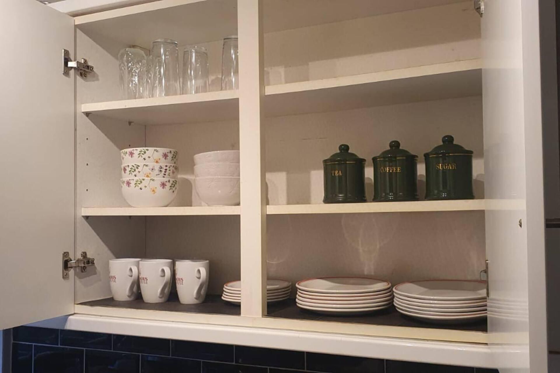 Un armario de cocina con estantes que contienen copas, cuencos, tazas y platos apilados.