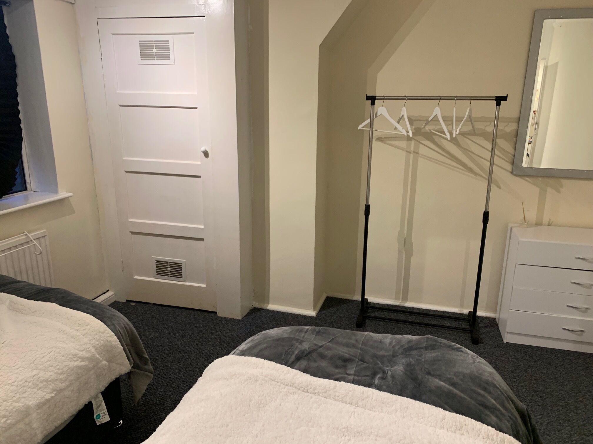 Un dormitorio con dos camas, un armario blanco, un radiador y una ventana con cortina.