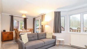Una sala moderna con un sofá gris, una mesita redonda pequeña, una silla de mimbre, un aparador de madera y una zona de comedor con una mesa y sillas.