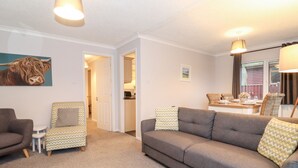 Una sala de estar con un sofá gris, sillones estampados y un comedor con una mesa dispuesta para cuatro.