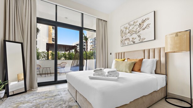A modern hotel room with a large bed, a view of the outdoor balcony, and a large window.