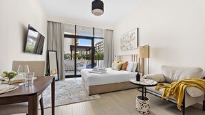 A modern hotel room with a bed, sofa, dining table, and a TV mounted on the wall.