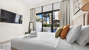 A modern hotel room with a large bed, a flat-screen TV, and a view of the outdoor area.