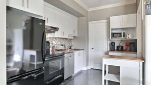 A modern kitchen with a stainless steel refrigerator, oven, microwave, and a coffee maker on the countertop. - L'Artiste | Chic condo à Québec by Alchalet (Quebec)