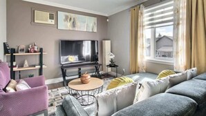 A living room with a sofa, armchair, TV, and a small table with a decorative item. - L'Artiste | Chic condo à Québec by Alchalet (Quebec)