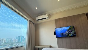 Quarto de hotel com uma cama grande, televisão fixada exibindo uma vista panorâmica, janela com cortinas e unidade de ar condicionado.