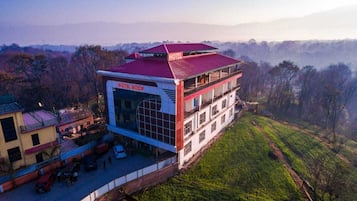 A hotel with a red roof and a large glass facade, surrounded by green hills and trees.