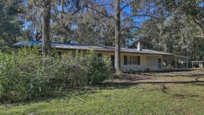 A single-story house with a covered porch, surrounded by dense trees and a grassy yard. - Pet-friendly Brooksville Cottage w/ Fire Pit! (Brooksville)