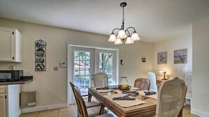 A dining area with a wooden table, chairs, and a chandelier. There are cabinets and a microwave in the kitchen area. - Pet-friendly Brooksville Cottage w/ Fire Pit! (Brooksville)