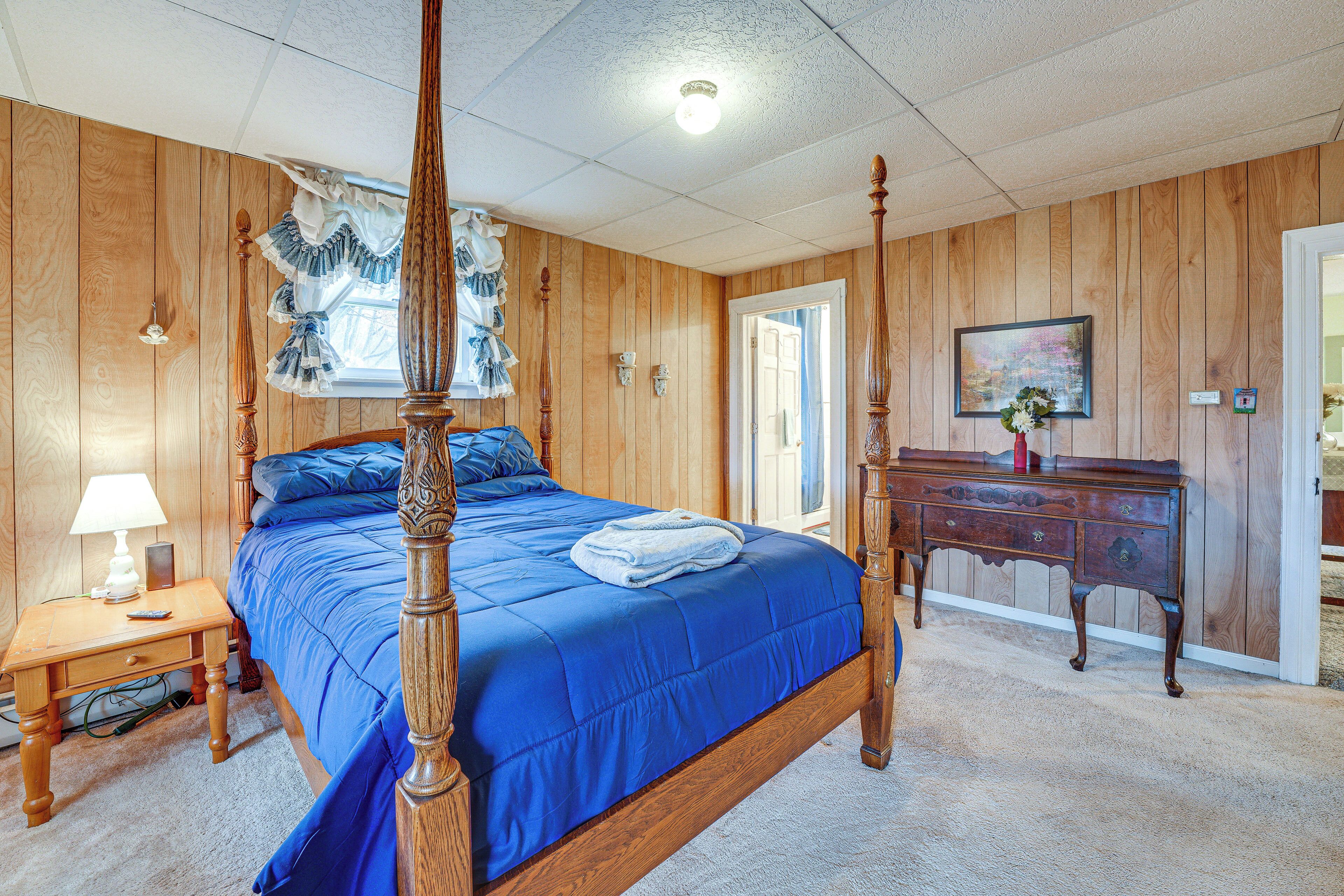 A bedroom with a four-poster bed, wooden walls, a dresser, and a nightstand with a lamp.