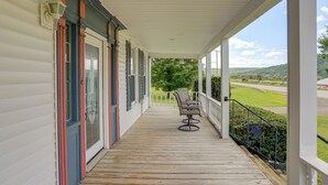 Eine überdachte Veranda mit Holzboden, einer Bank und Blick auf eine grüne Landschaft.
