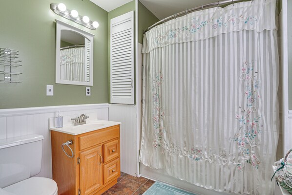 A bathroom with a wooden vanity, a white sink, a mirror with lights, and a shower curtain with floral embroidery.