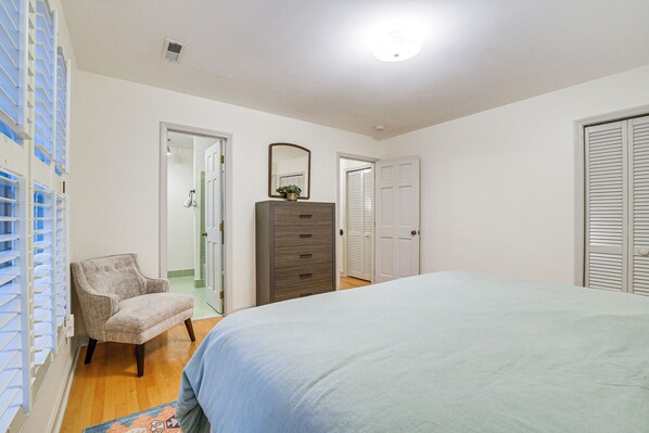 A bedroom with a bed, a dresser, a chair, and a door leading to another room.