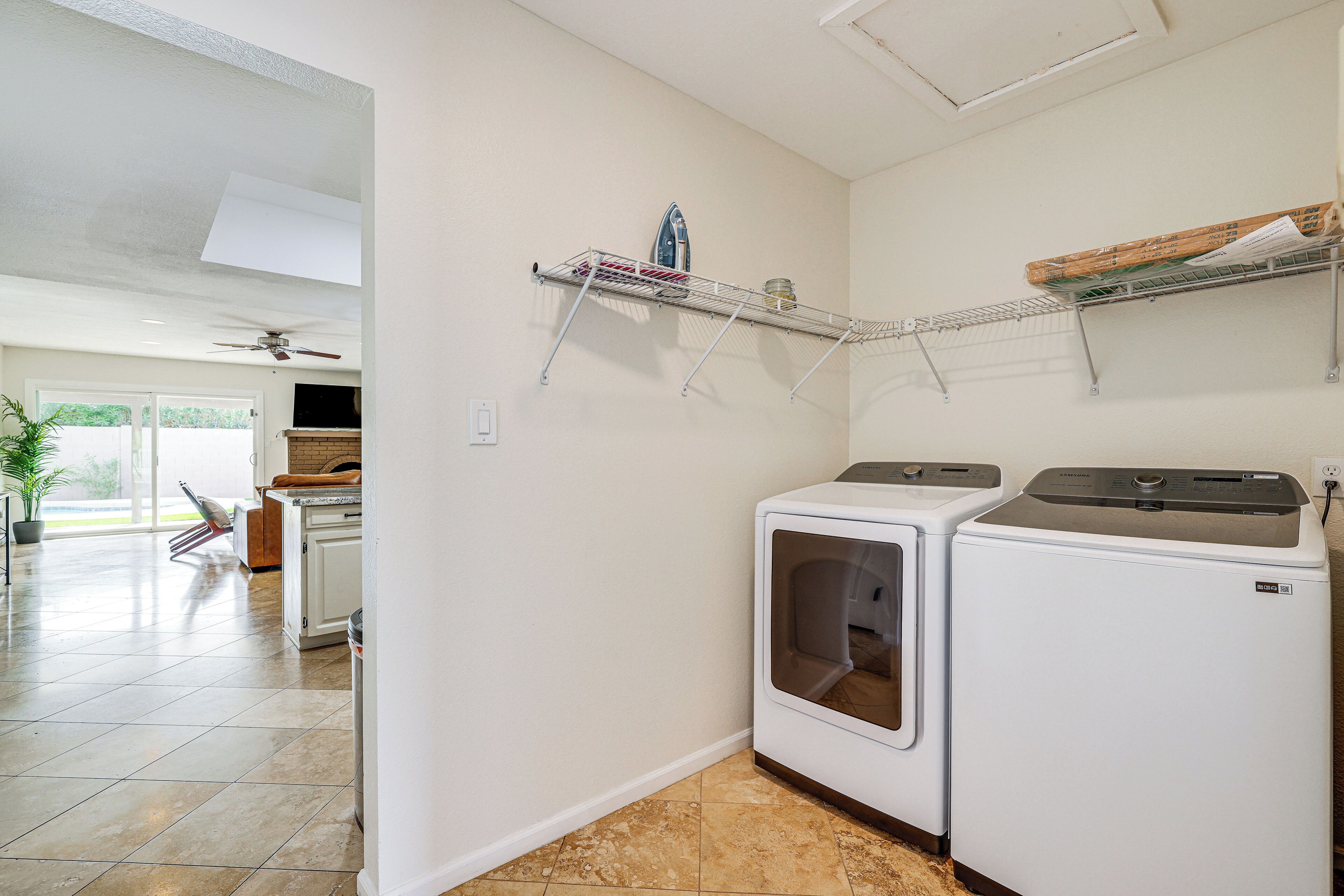 A laundry room with two stacked washers and dryers, metal shelves above, and a potted plant in the background.