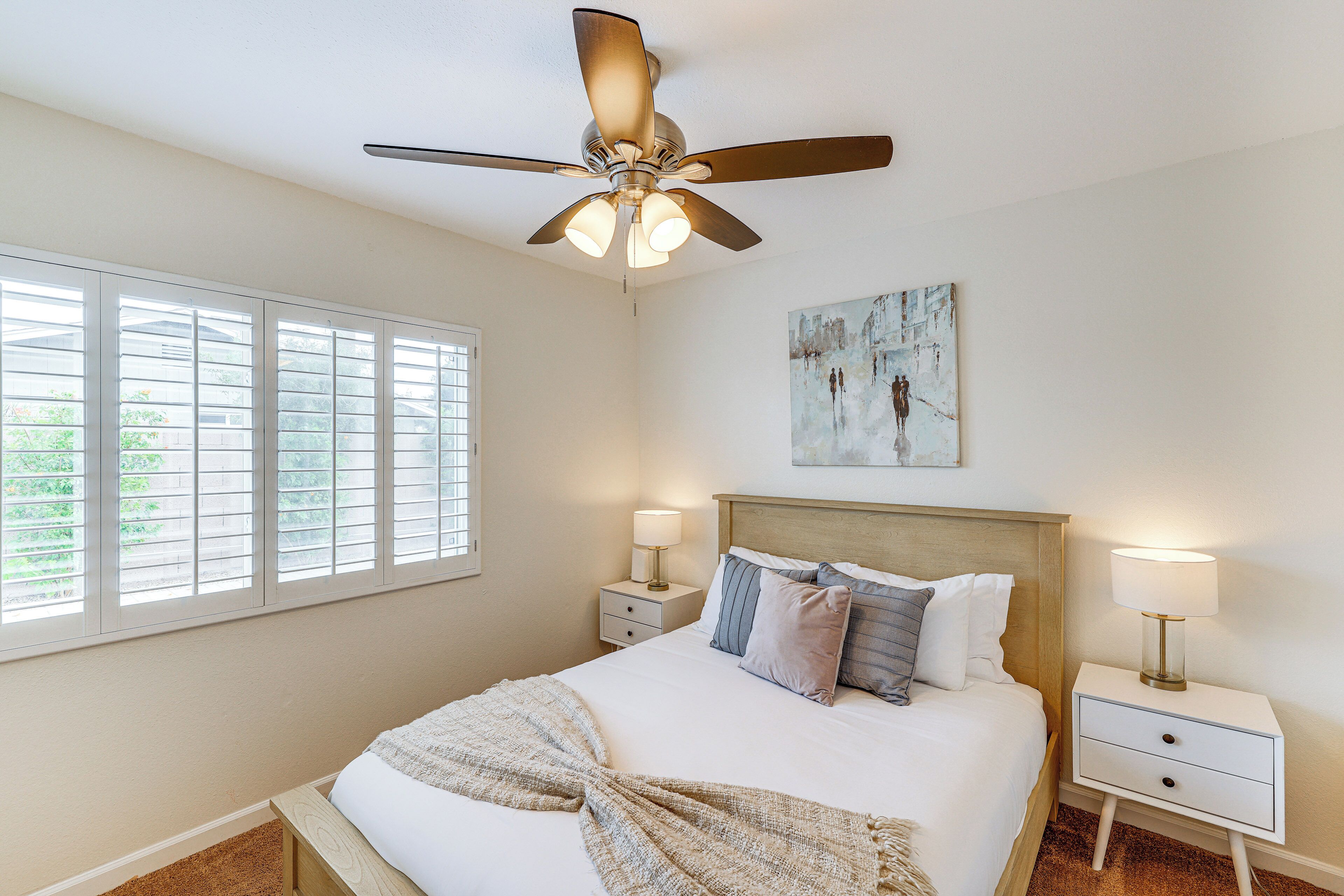 A bedroom with a bed, two bedside tables, a ceiling fan, and a window with blinds.
