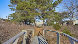 A wooden boardwalk leading to a building surrounded by trees and dry vegetation. - Private Dock: Fisherman's Paradise on Bass River (West Dennis)
