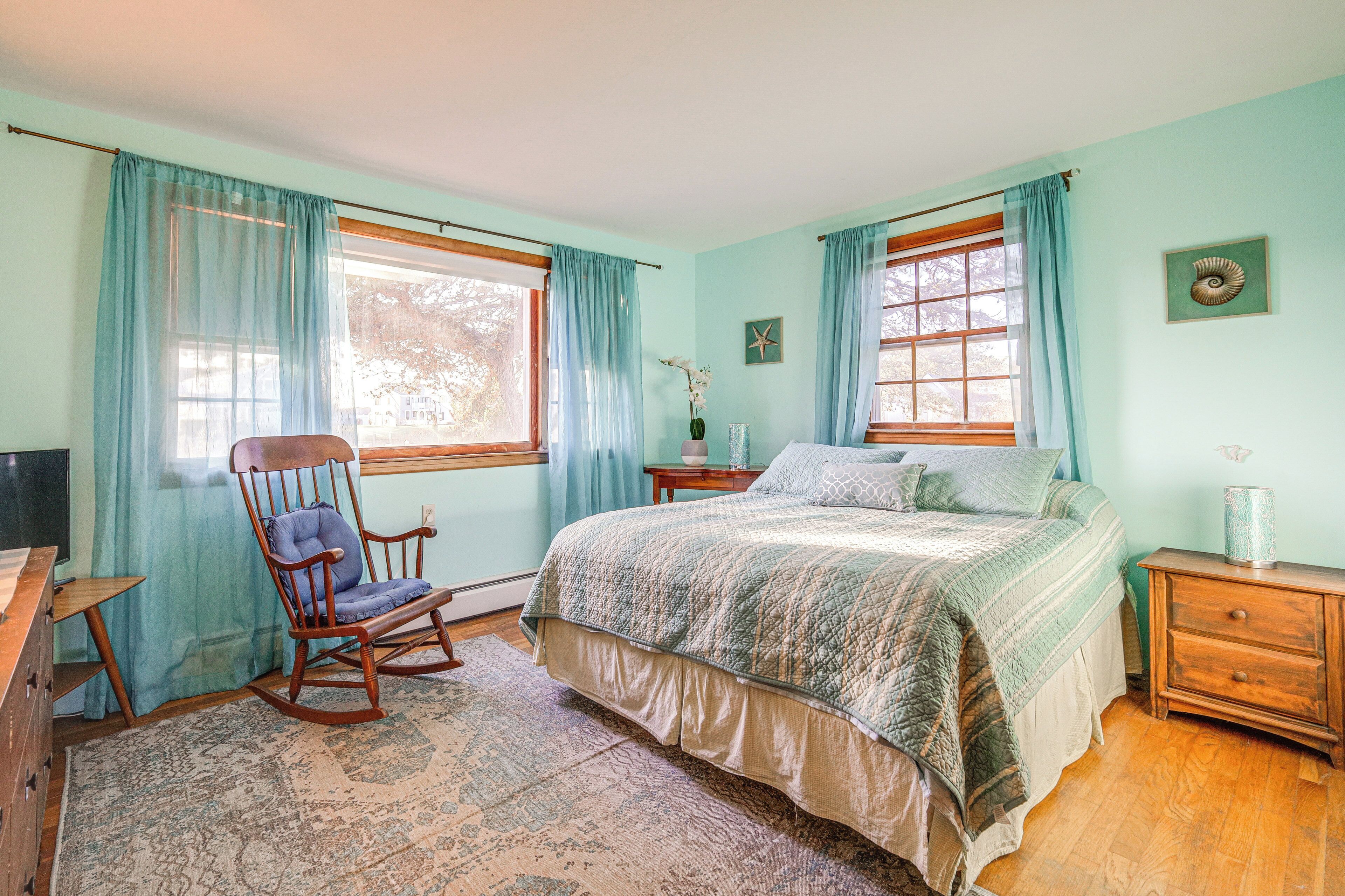 A bedroom with a large bed, a rocking chair, a wooden dresser, and a nightstand.