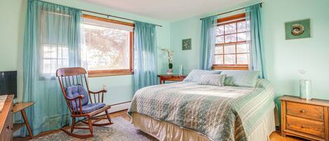 A bedroom with a large bed, a rocking chair, a wooden dresser, and a nightstand.