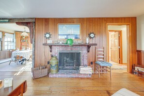 A room with a fireplace, wooden walls, a dining table with chairs, and a view of the outside. - Private Dock: Fisherman's Paradise on Bass River (West Dennis)