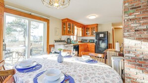 A kitchen with wooden cabinets, a refrigerator, and a dining area with a table set for two. - Private Dock: Fisherman's Paradise on Bass River (West Dennis)