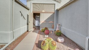 A narrow courtyard with a white wall, a garage door, and a small door leading to a garage. There are several cacti and decorative pots on the ground. - Green Valley Getaway Near Golfing: Pool Access! (Green Valley)