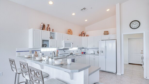 A modern kitchen with white cabinets, a central island with bar stools, and various kitchen appliances. - Green Valley Getaway Near Golfing: Pool Access! (Green Valley)