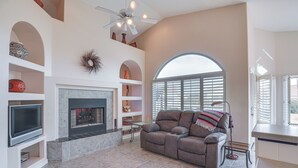 A living room with a fireplace, a sofa, a TV, and a ceiling fan. - Green Valley Getaway Near Golfing: Pool Access! (Green Valley)