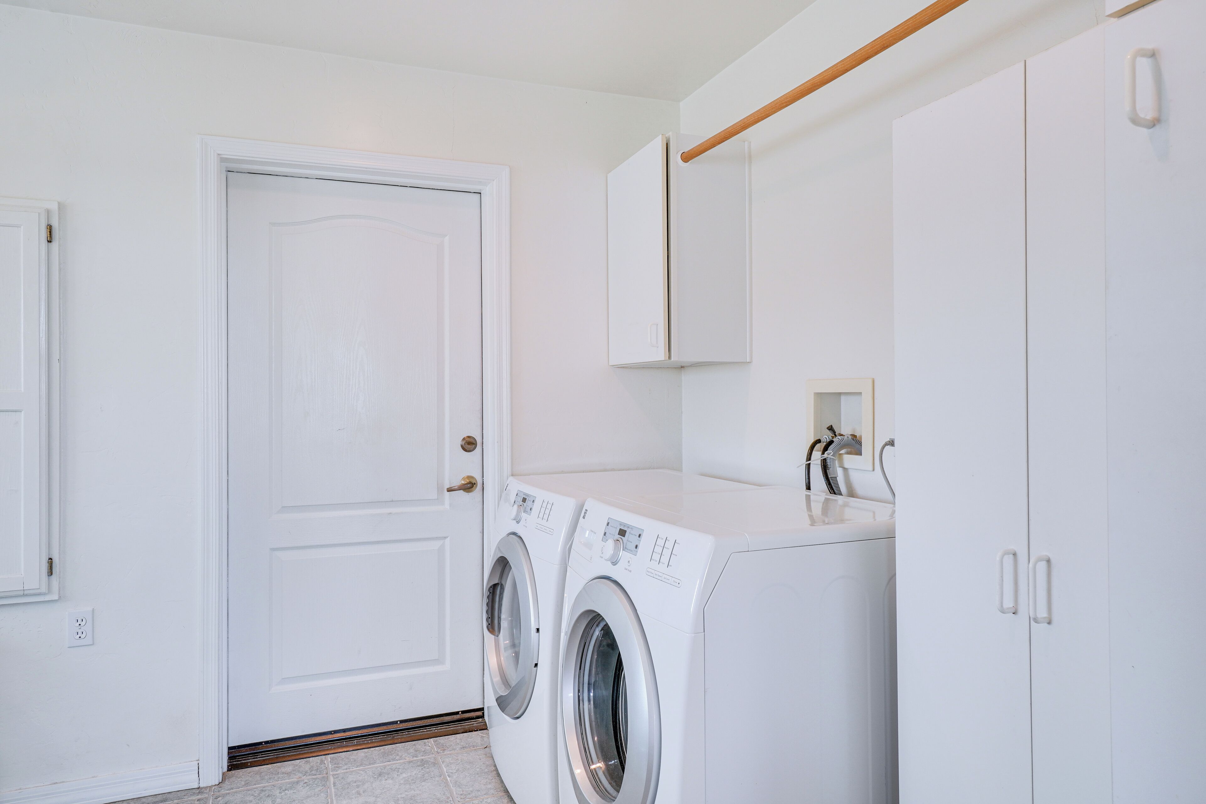 A laundry room with two front-loading washing machines, a sink, and a cabinet.