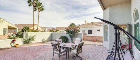 A patio with a table and chairs, a swing, and a view of neighboring houses and palm trees.