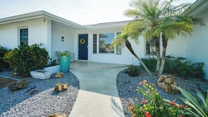 A modern house with a front porch, a blue door, and a small garden with rocks and plants.
