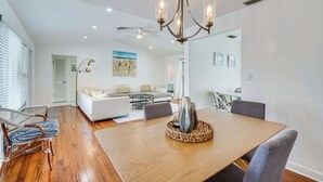 A spacious living room with a wooden dining table, gray upholstered chairs, and a chandelier.