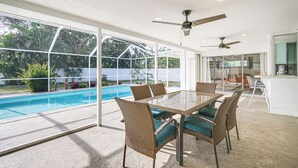 A glass-enclosed patio with a pool, wicker furniture, ceiling fans, and a view of the outdoors.