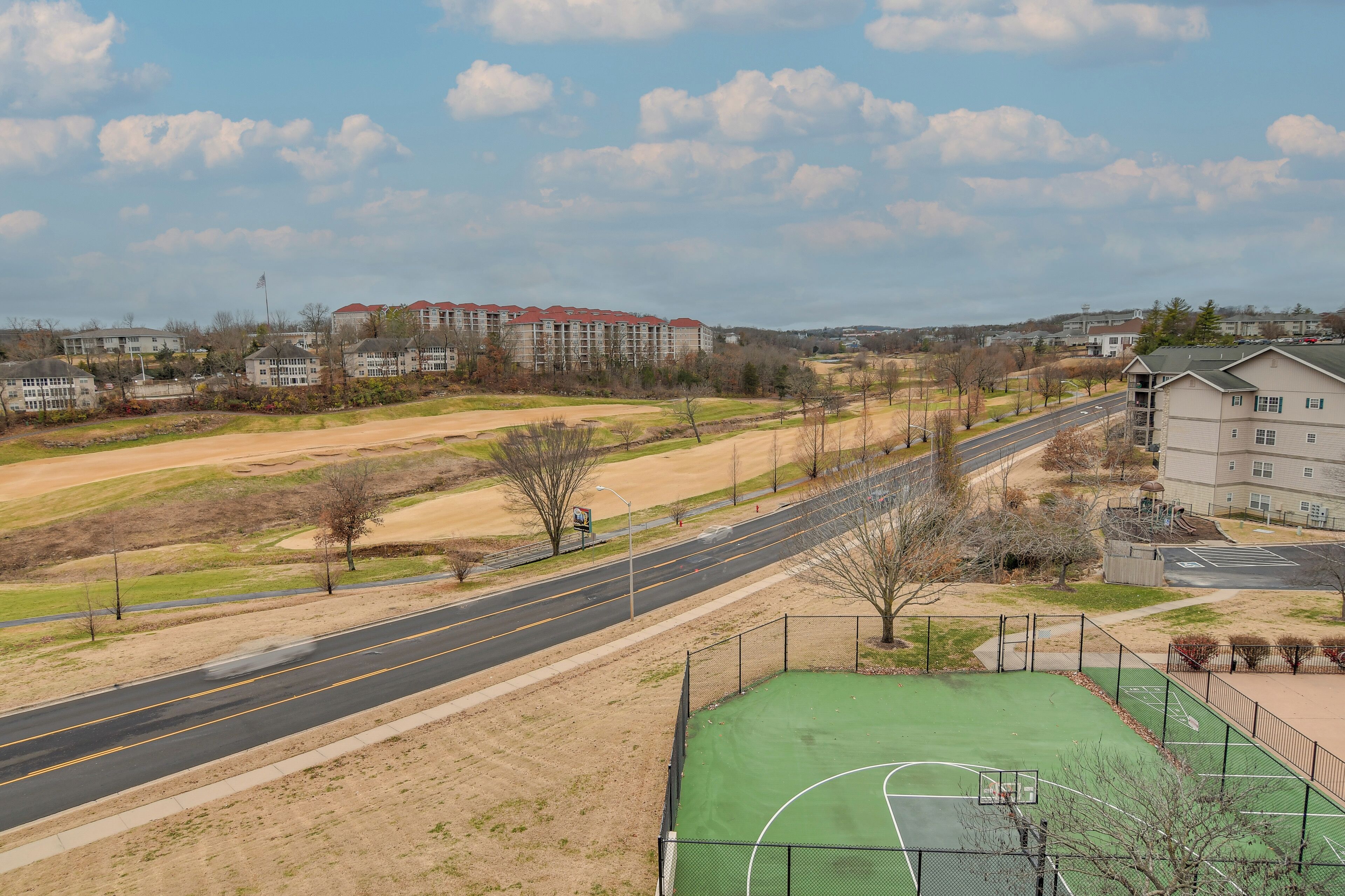 Un terrain de basket situé à côté d’une route, avec des bâtiments en arrière-plan.