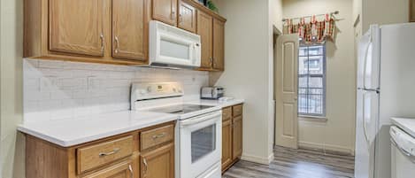 Una cocina con armarios de madera, un microondas blanco, una estufa y un refrigerador.