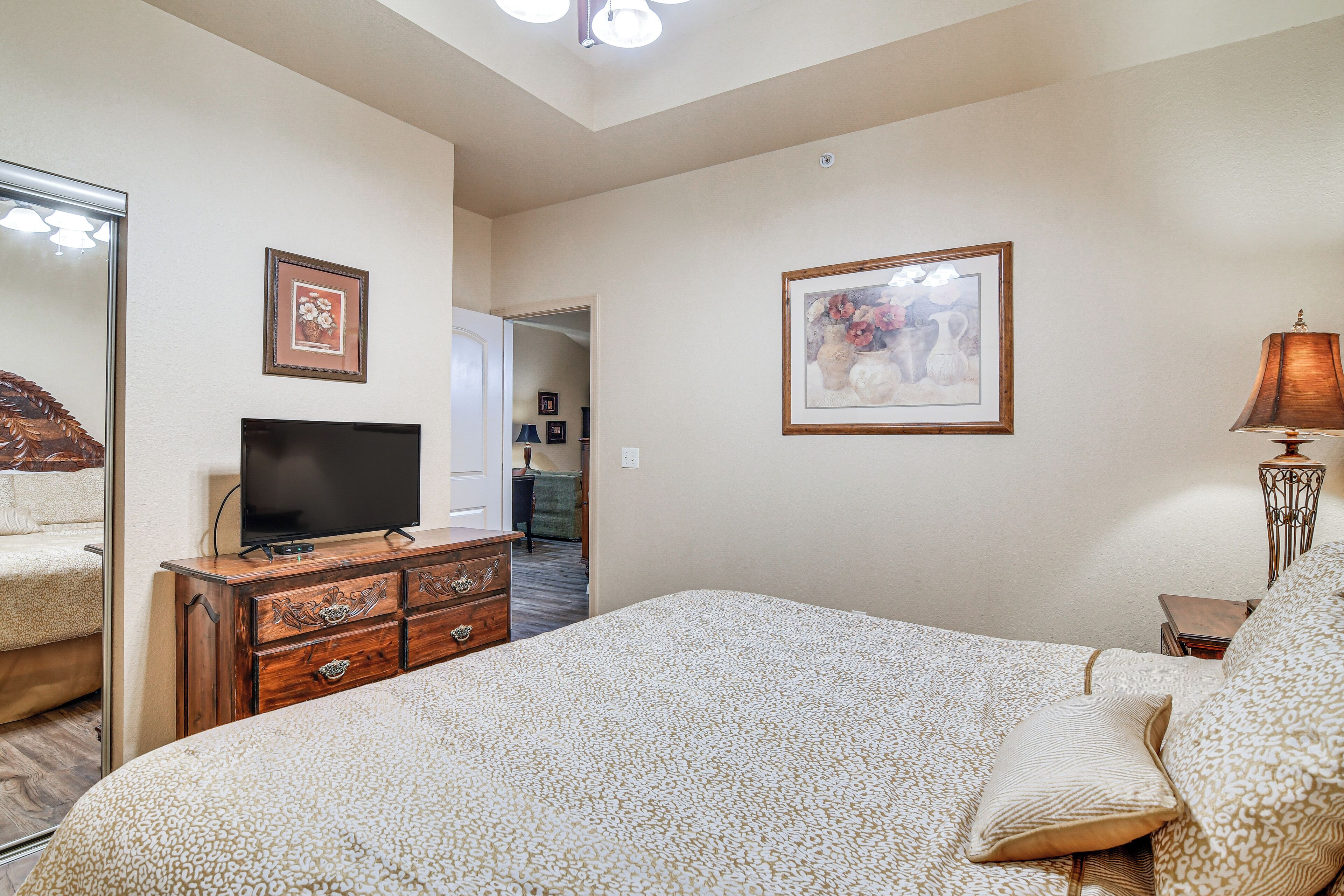 A bedroom with a large bed, a dresser with drawers, a flat-screen TV, and two framed pictures on the wall.
