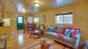 A cozy cabin interior with a wooden ceiling, a sofa, a dining table with chairs, and a kitchen area. - Peaceful Beattyville Cabin Near Red River Gorge! (Beattyville)